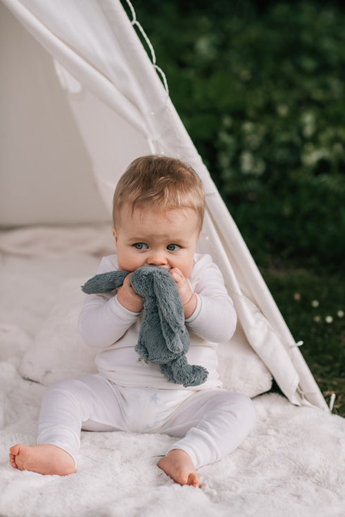 Baby wearing merino pyjamas holding a soft bunny to his mouth